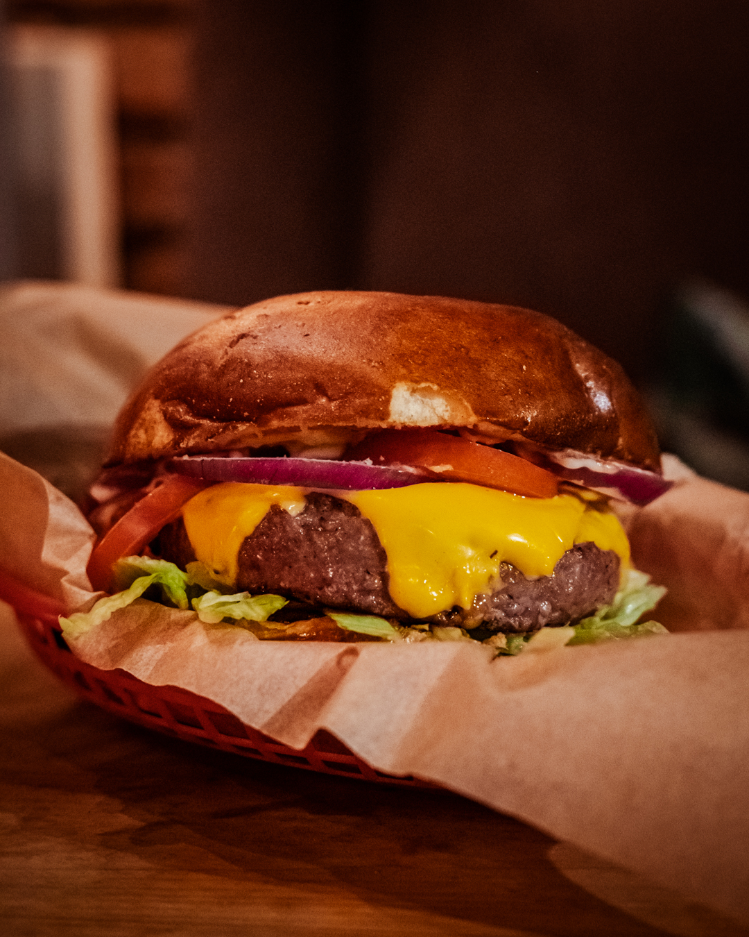 A cheeseburger with red onion, tomato and lettuce in a basket